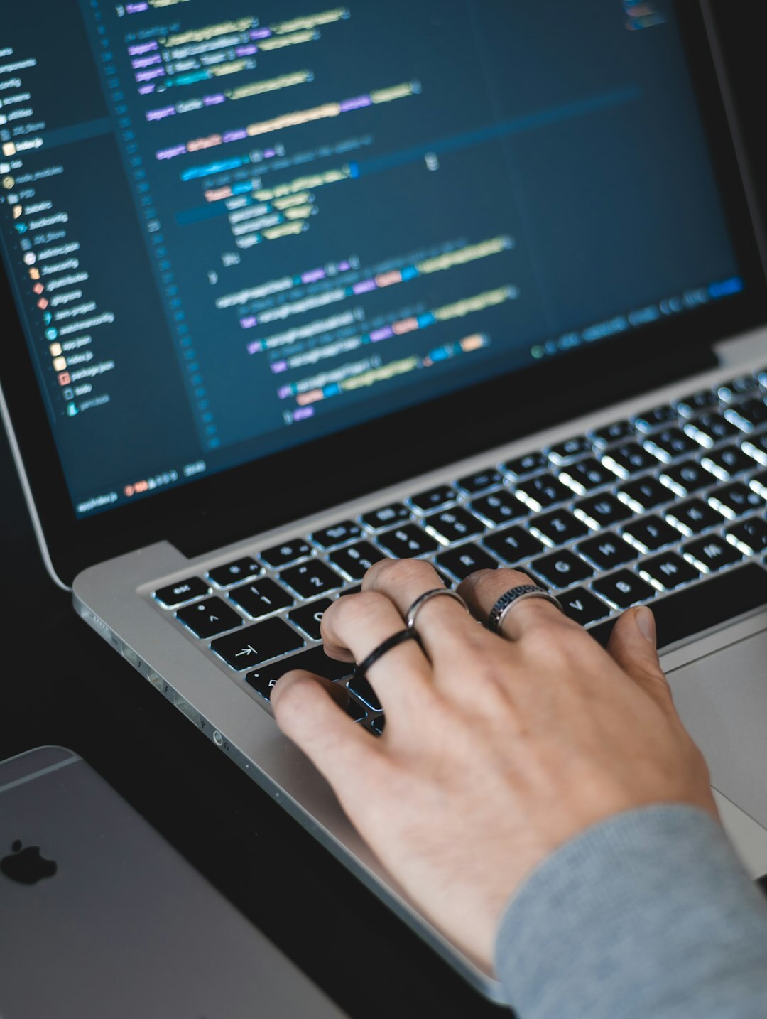 Close up of hands typing on a laptop keyboard with code on screen